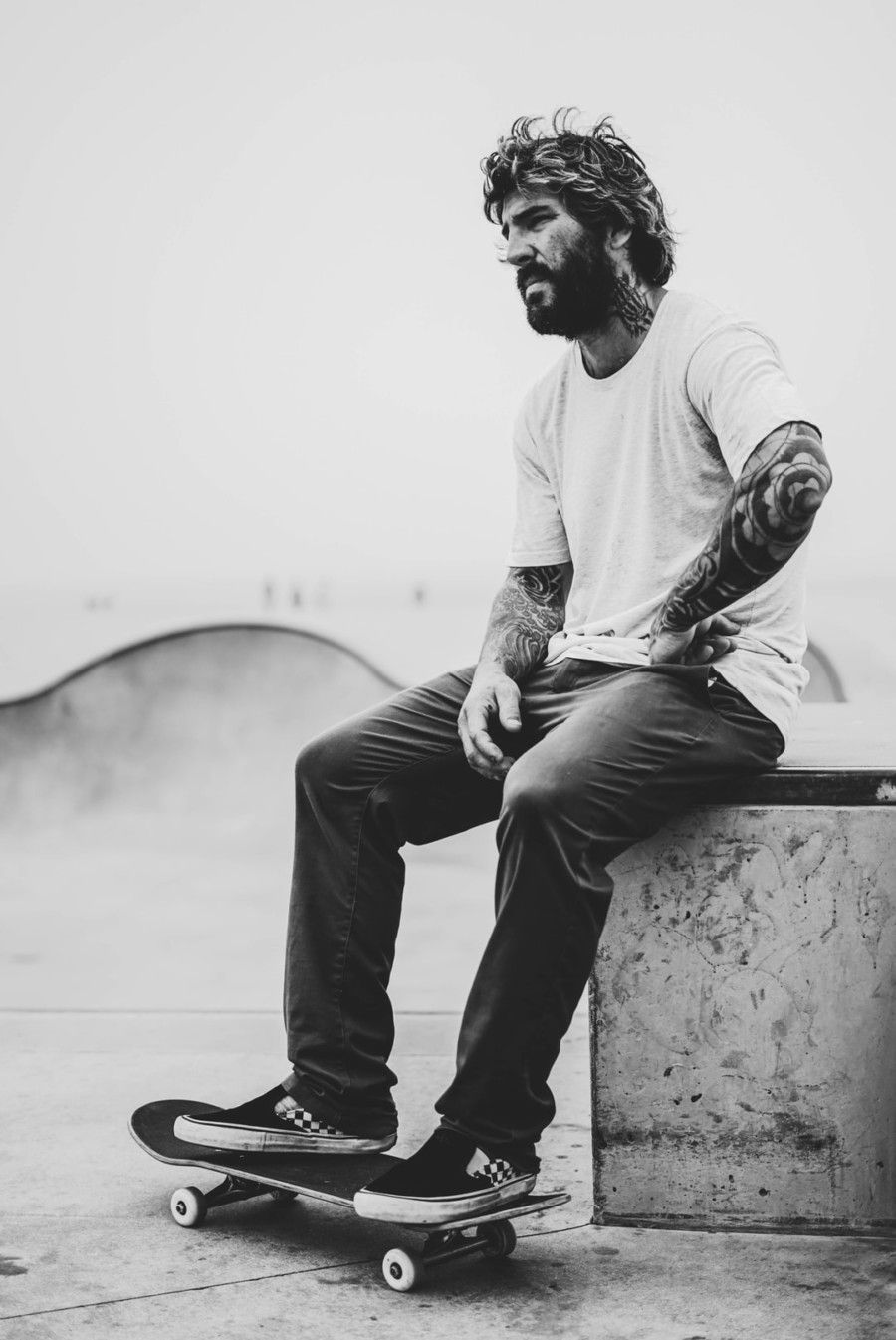 grayscale-photography-of-man-sitting-on-bench-while-his-feet-on-skateboard