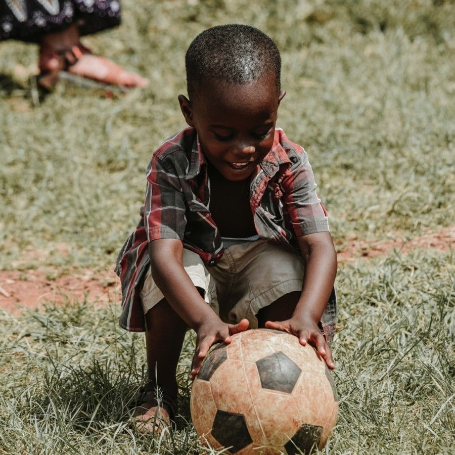 smiling-boy-sitting-while-holding-soccer-ball-at-daytime
