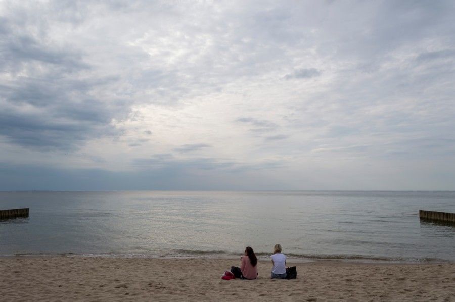 two-women-sitting-on-sand-near-seashore