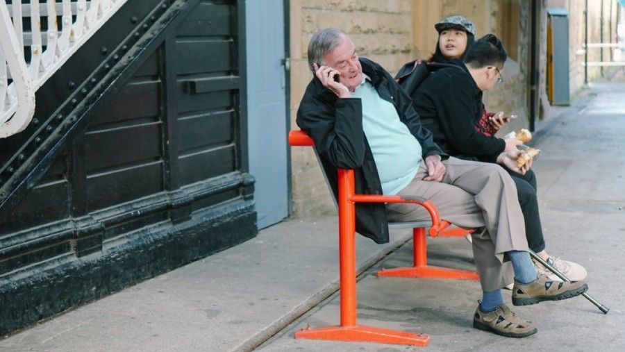 man-using-smartphone-while-sitting-on-orange-metal-chair